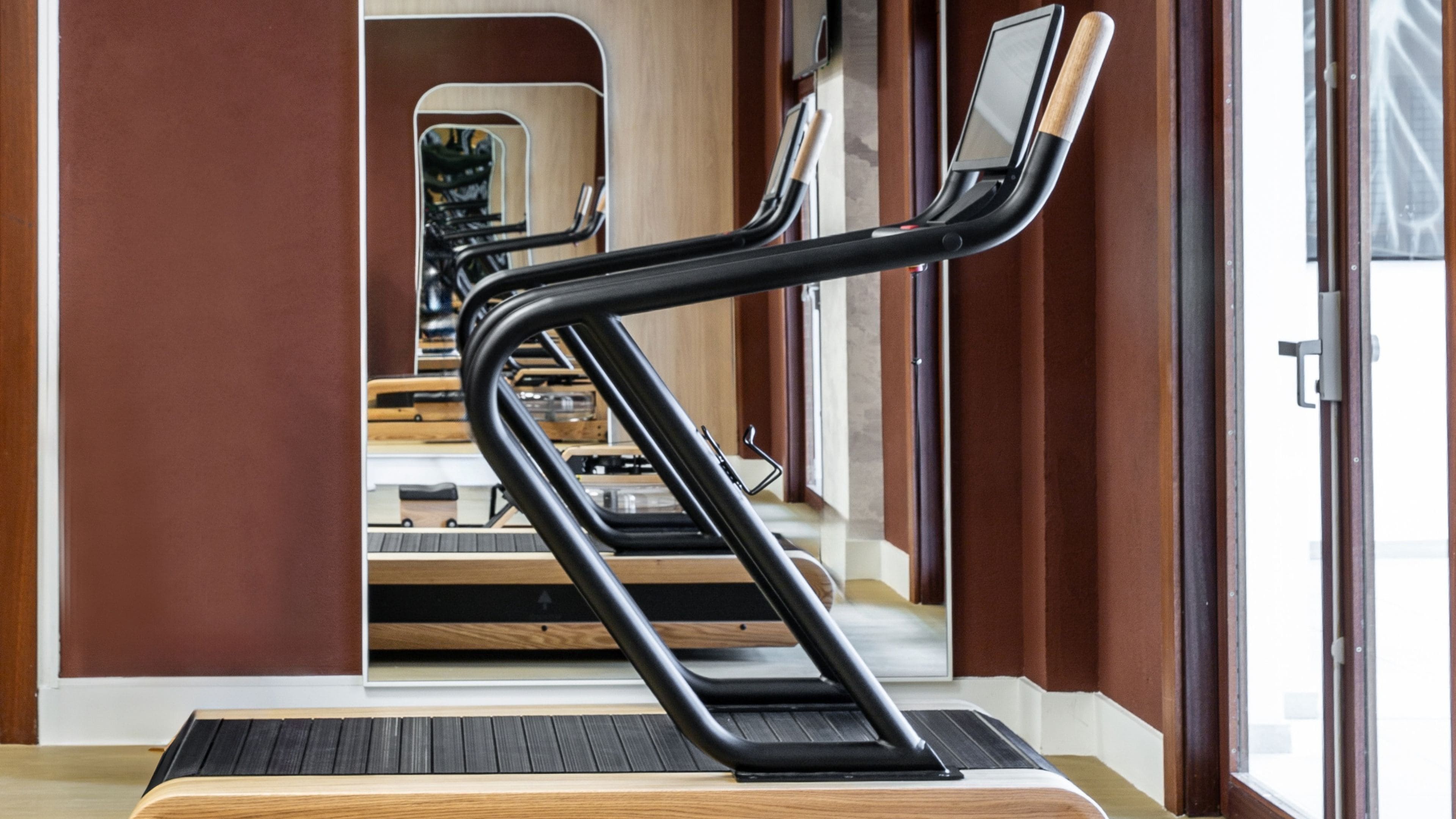 A modern gym with a treadmill, mirrored wall, and wooden flooring.