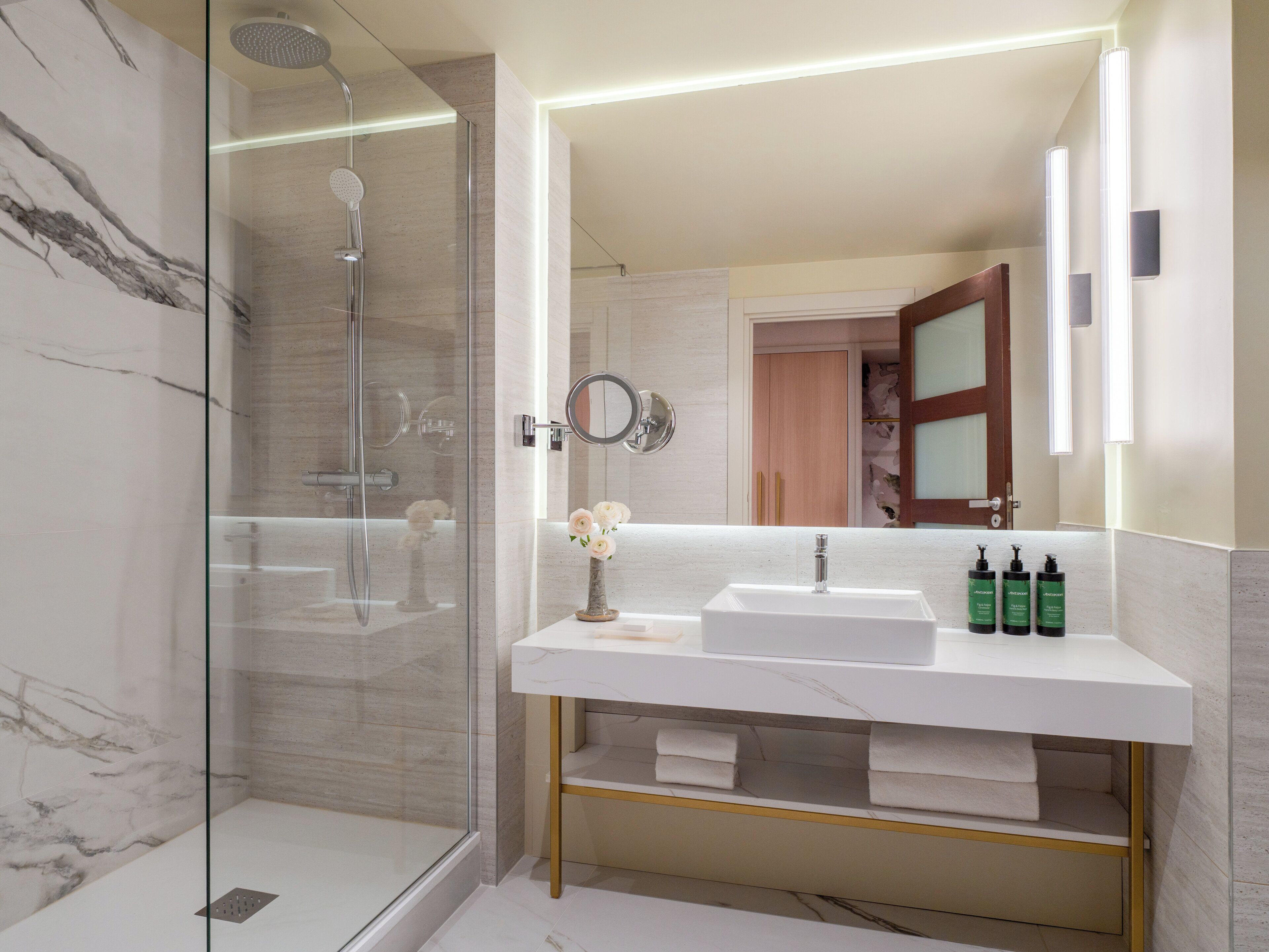 Een moderne badkamer met een douchecabine van glas, een wit marmeren wastafel en een spiegel met ingebouwde verlichting.