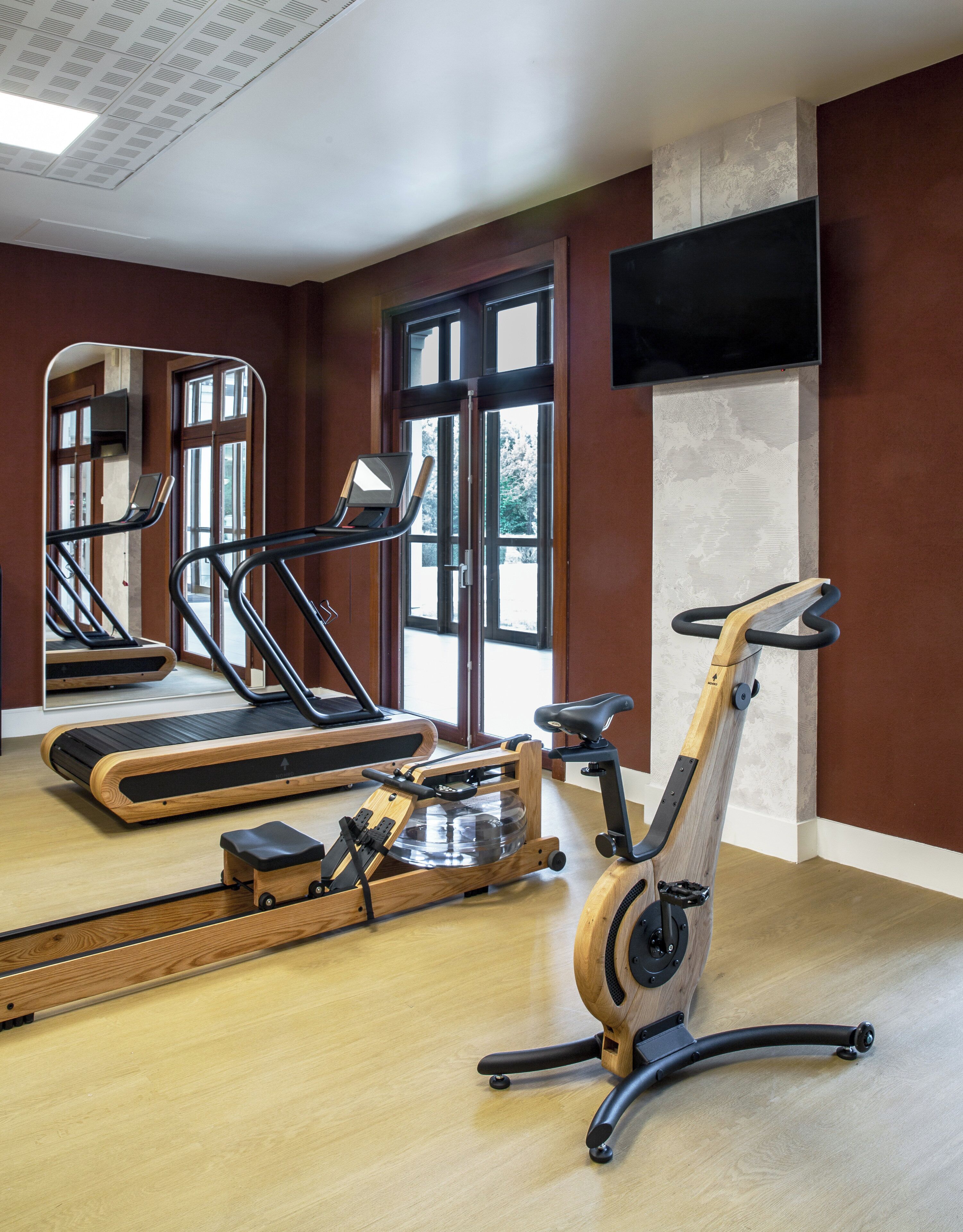 Un gimnasio con máquinas de cardio, una máquina de remo y un televisor montado en la pared.