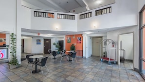 A spacious indoor area with multiple seating arrangements, a service cart, and a visible exit door. - Motel 6 Lawrence, KS (Lawrence)
