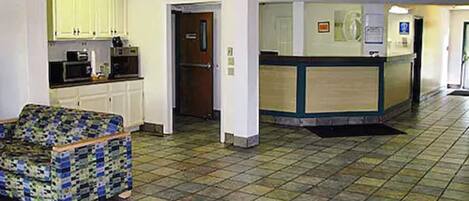 A hotel lobby with a reception desk, a kitchenette, and a patterned armchair.