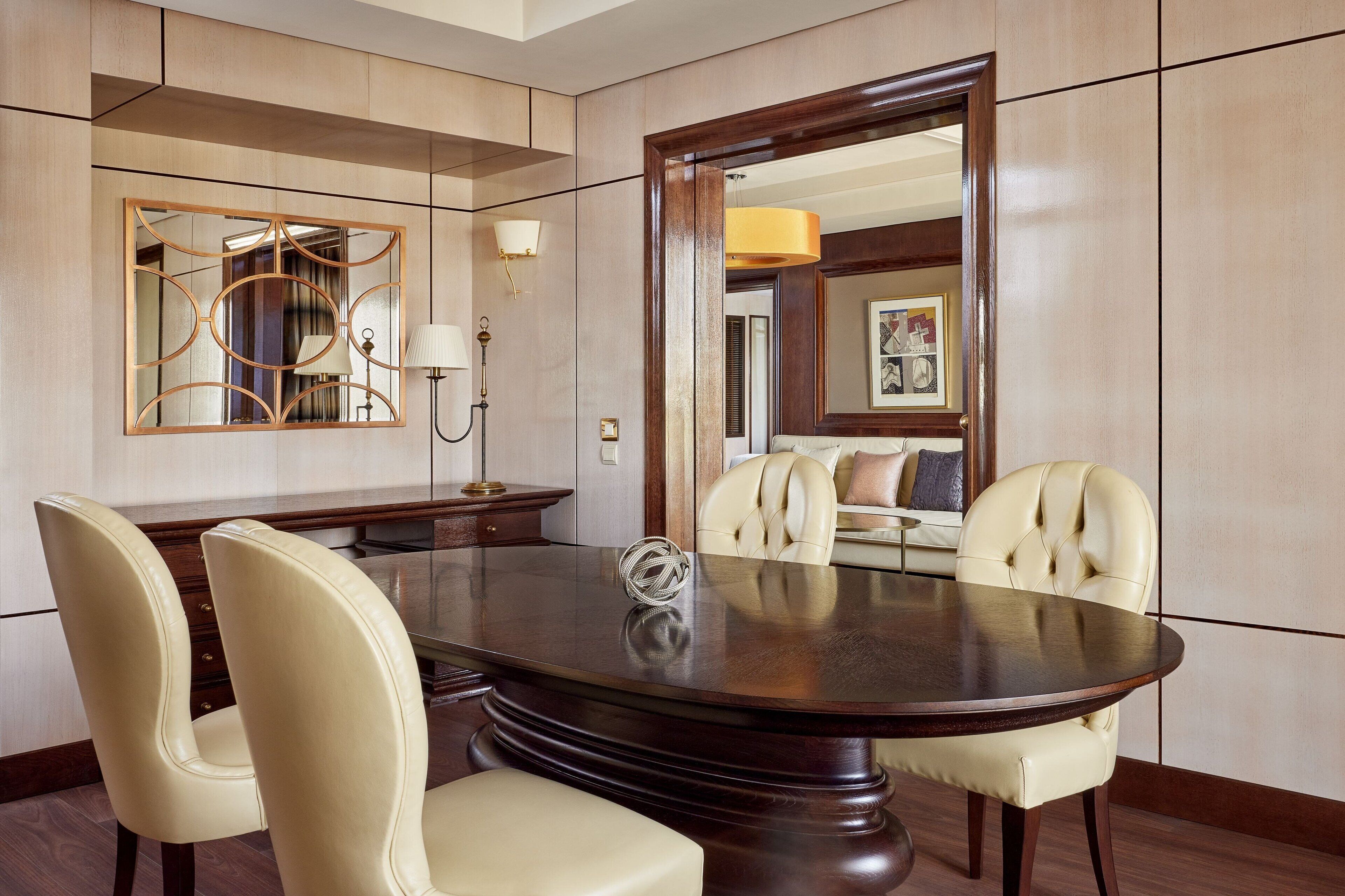 Une salle de conférence équipée d’une table ronde, de quatre chaises, d’un grand miroir et d’une lampe fixée au mur.