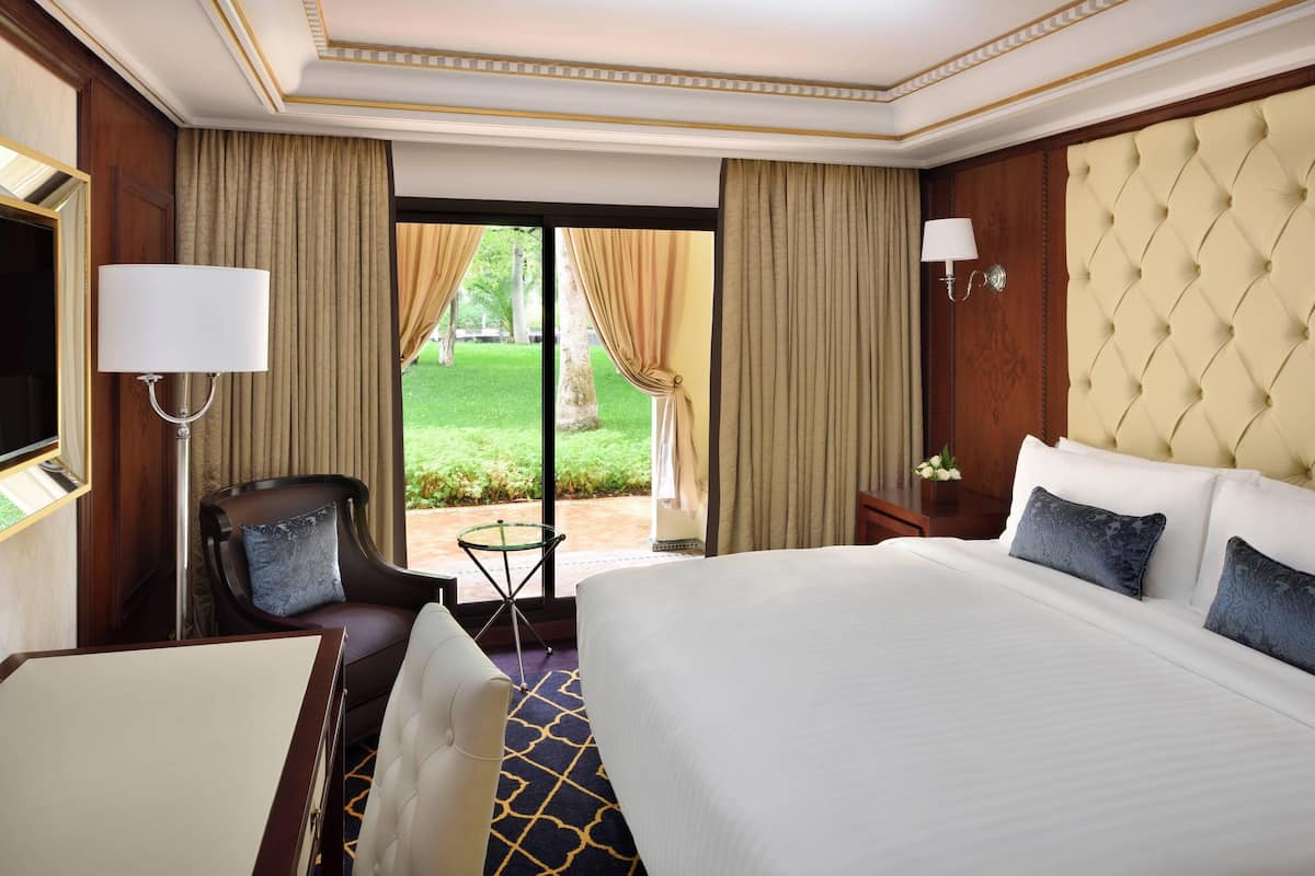 A hotel room with a large bed, a chair, a small table, and a view of the outdoors.
