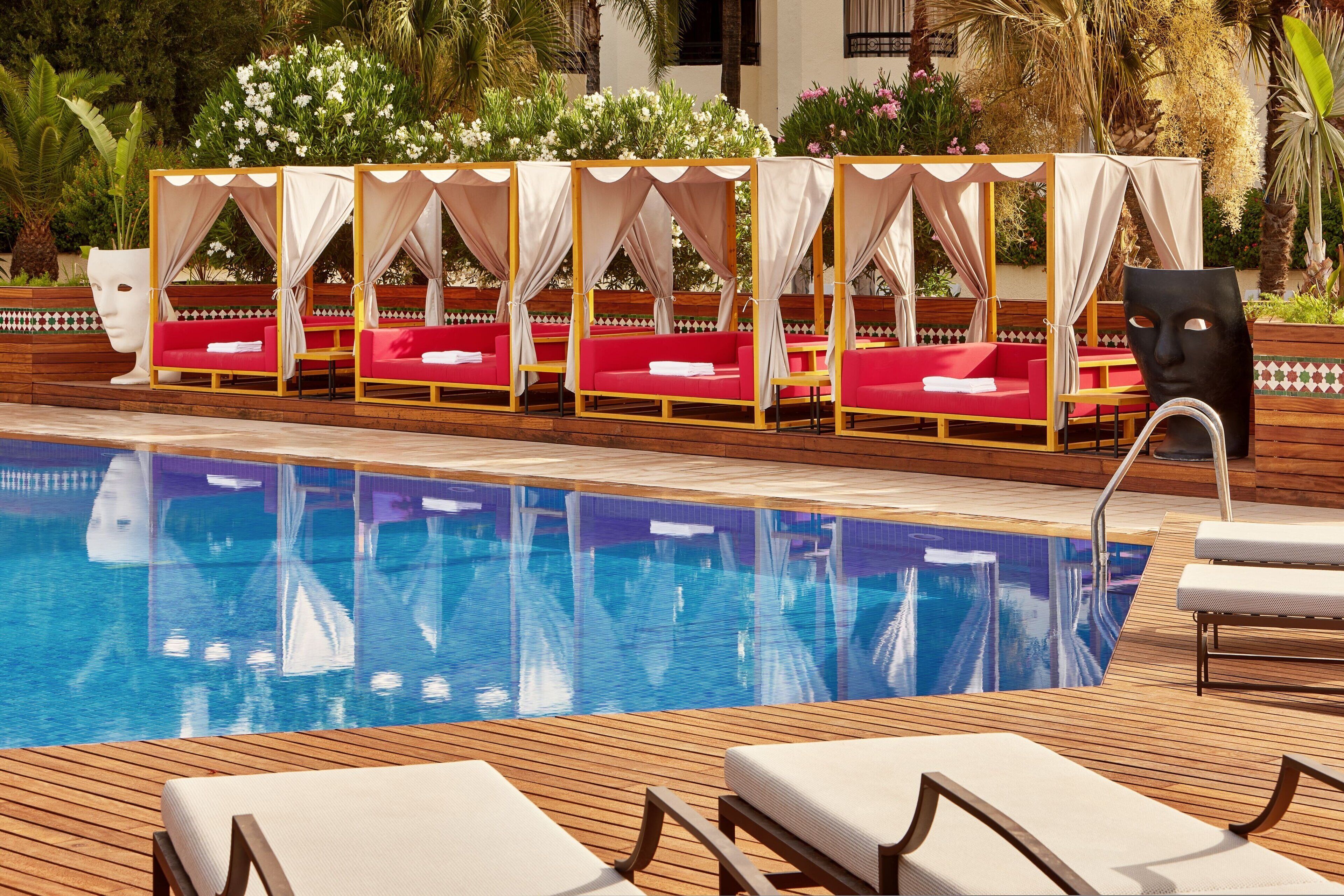 Un espace aménagé au bord de la piscine, avec une rangée de chaises rouges dotées de coussins et une terrasse en bois.