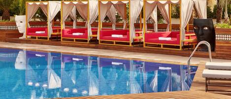 A poolside area with a row of red cushioned chairs and a wooden deck.