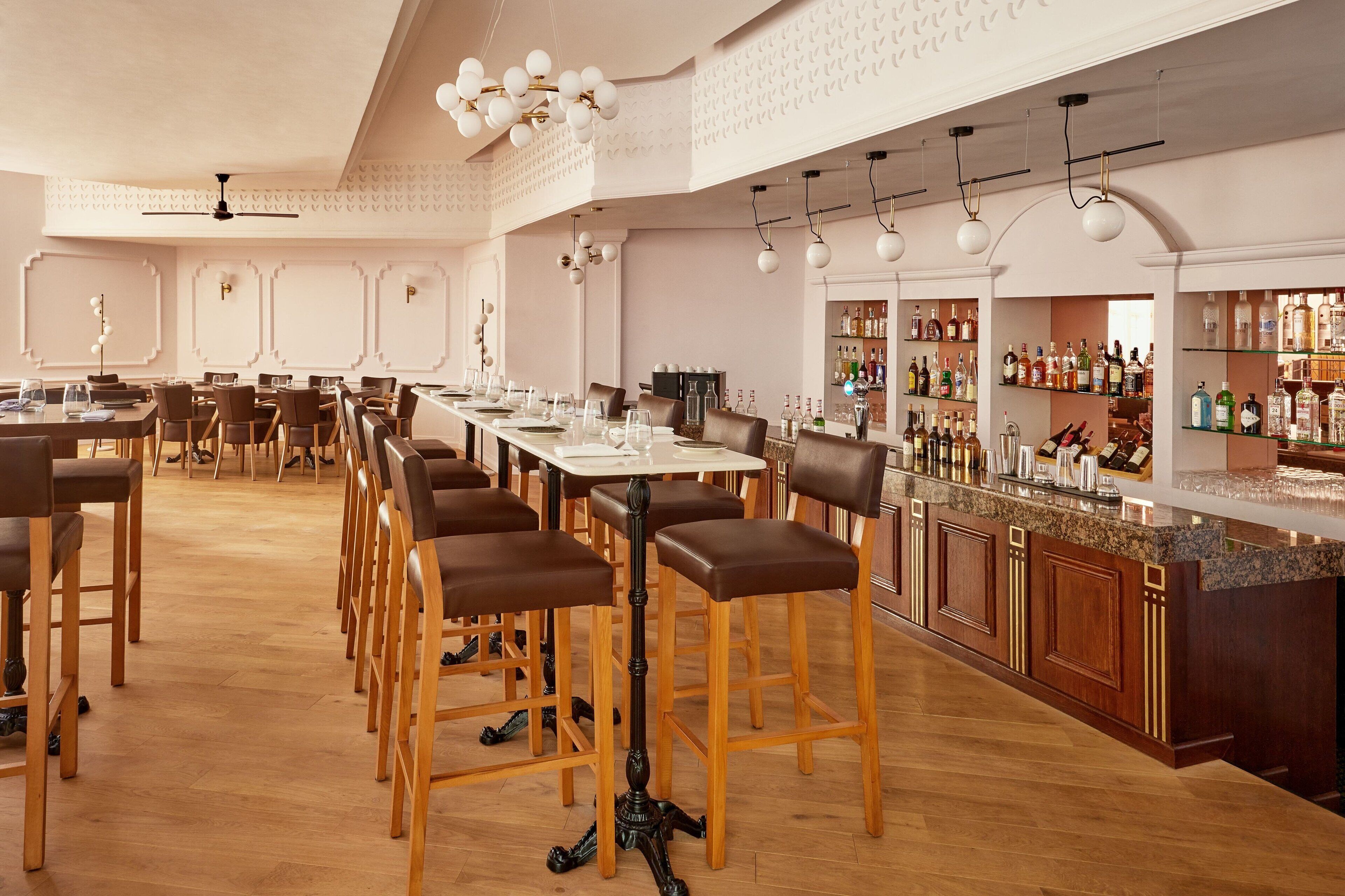 A spacious bar area with wooden bar stools and a long counter, surrounded by shelves of bottles.