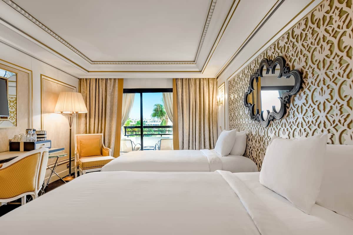 A hotel room with two beds, a desk with a chair, a lamp, and a decorative mirror.