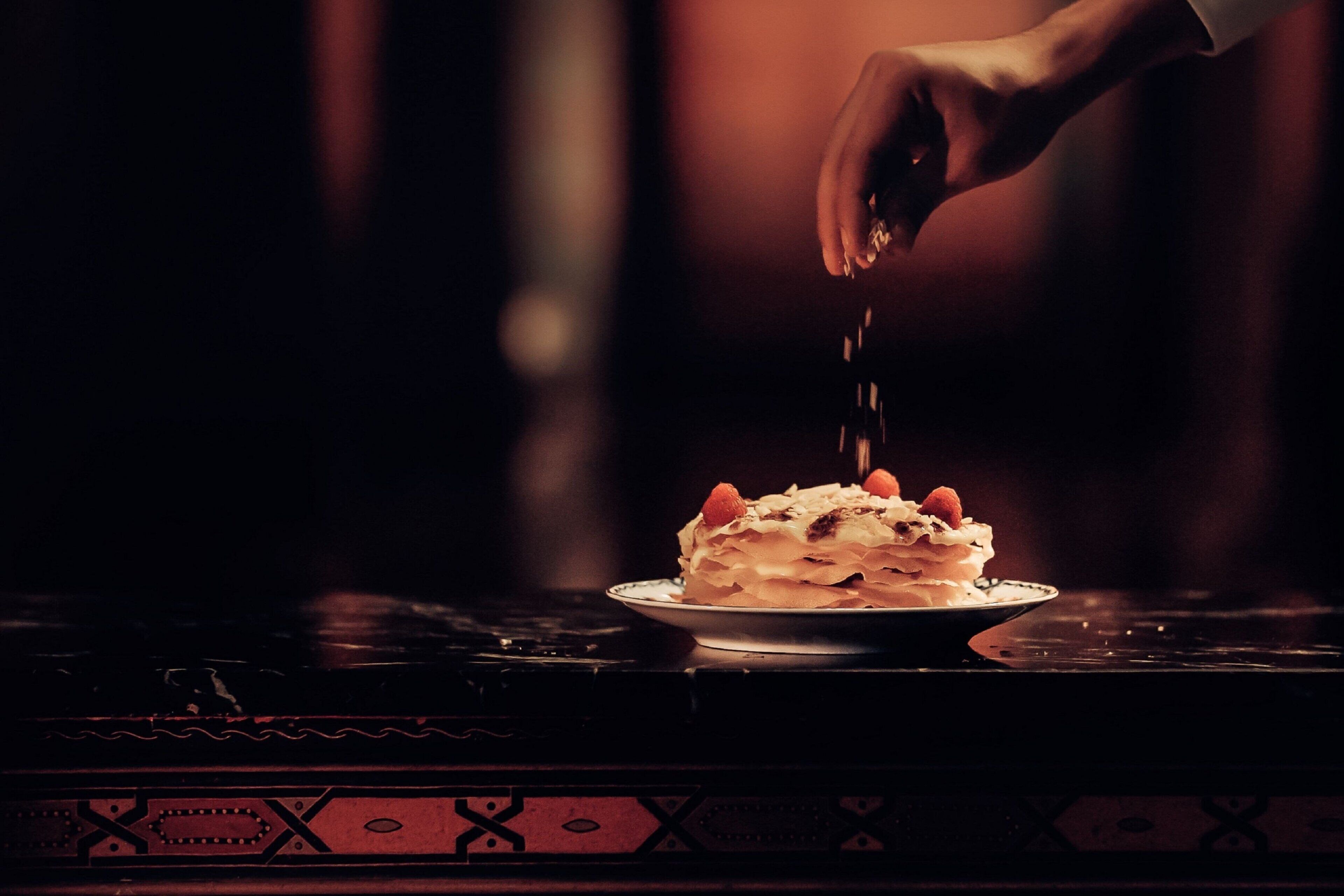 Iemand strooit poedersuiker over een dessert op een bord.