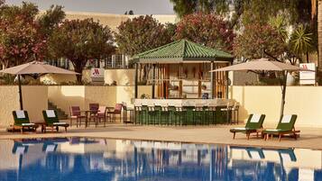 A pool area with lounge chairs and umbrellas, a bar, and a gazebo.