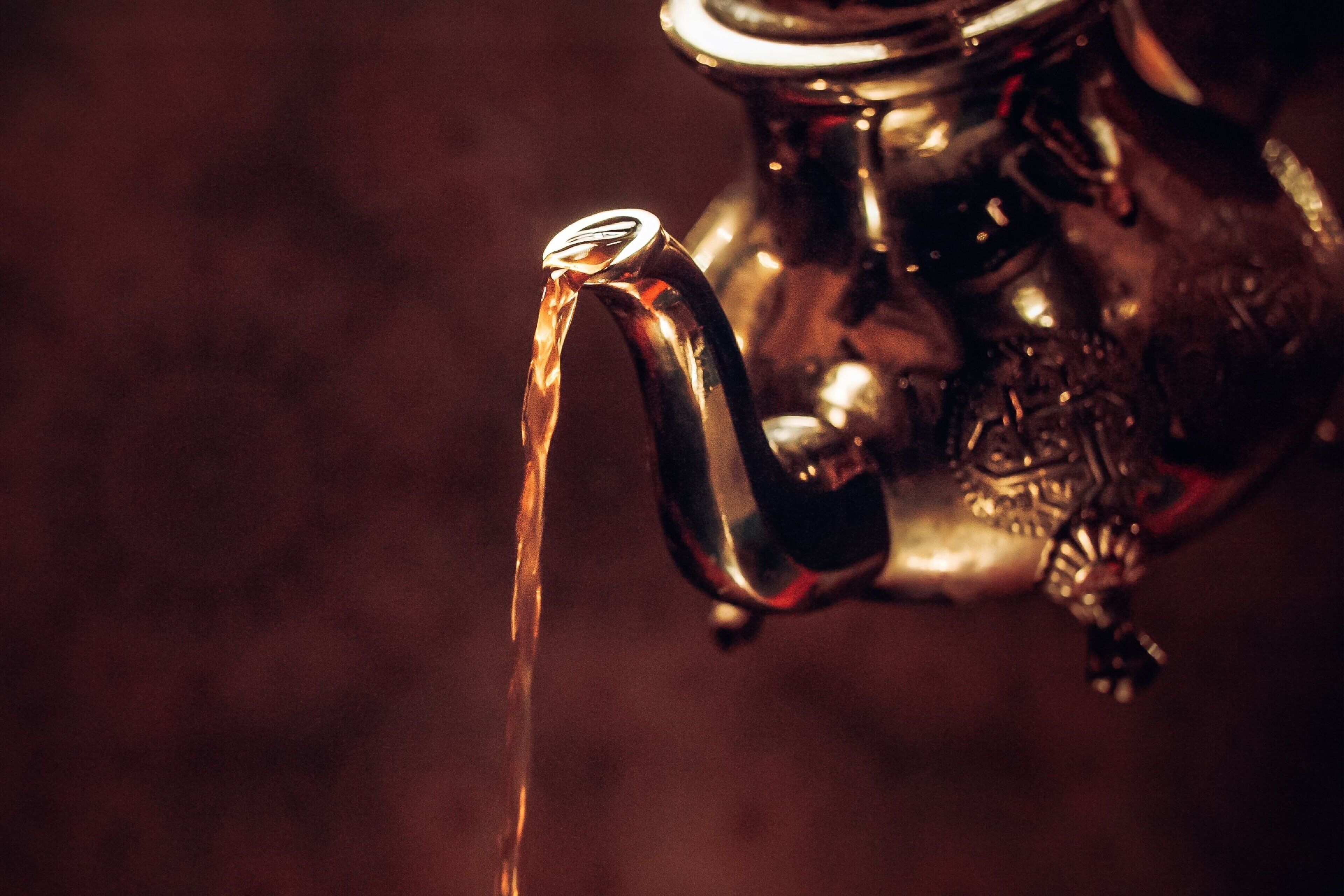 A close-up of a metallic teapot with a spout from which water is flowing.