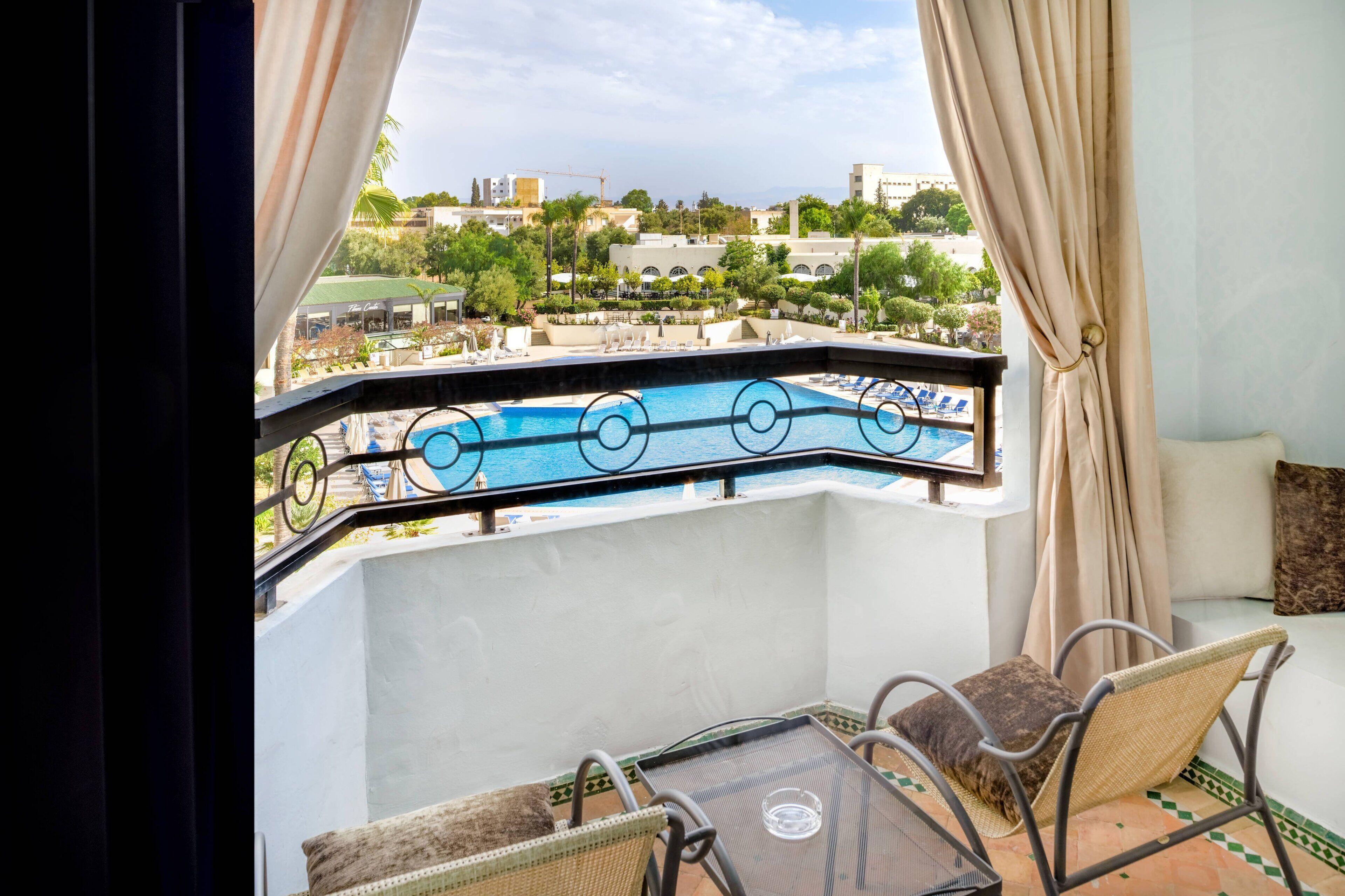 A balcony with a view of a pool and cityscape.