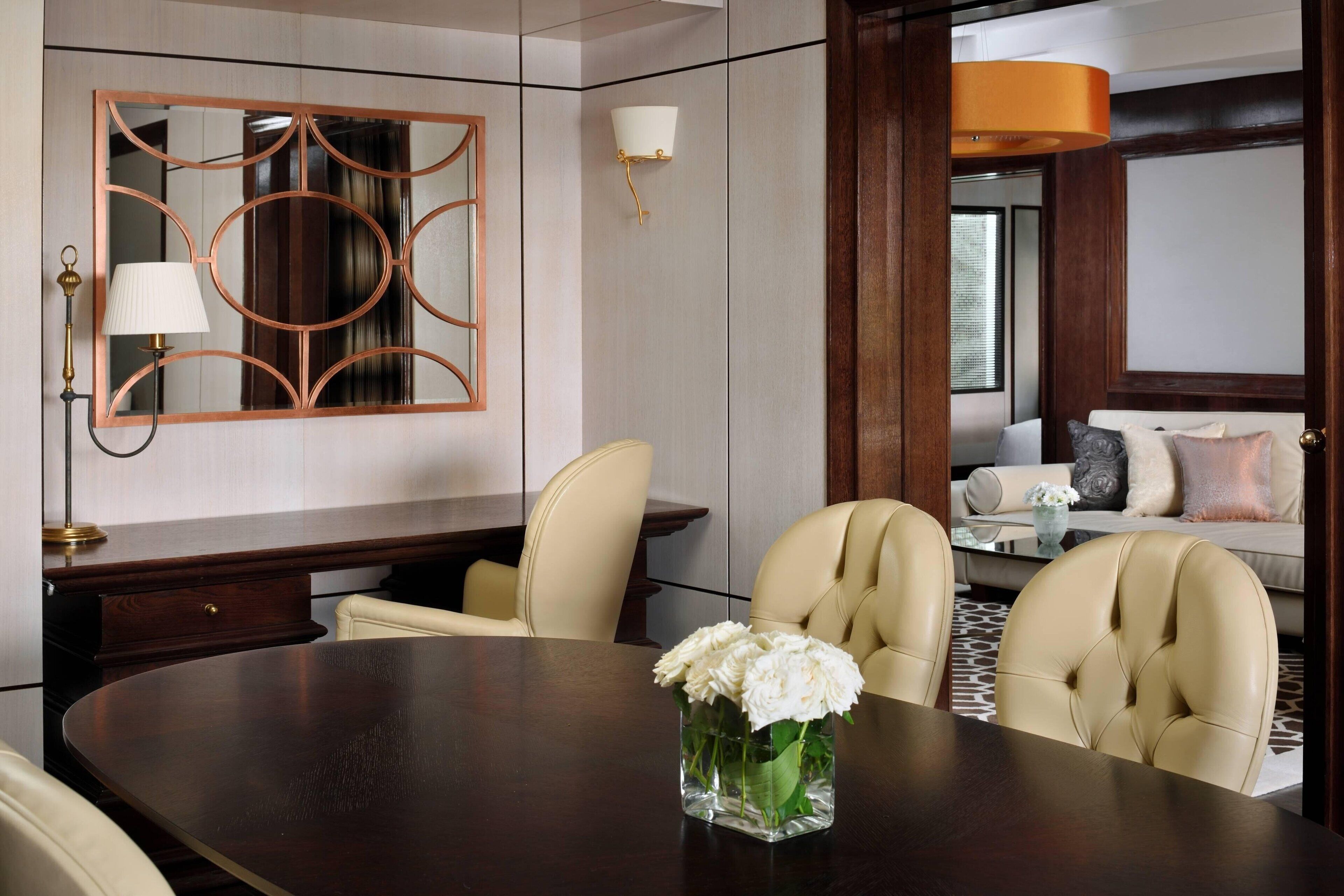Un coin repas moderne avec une table ronde, deux chaises, un vase de fleurs, un miroir mural et un canapé en arrière-plan.