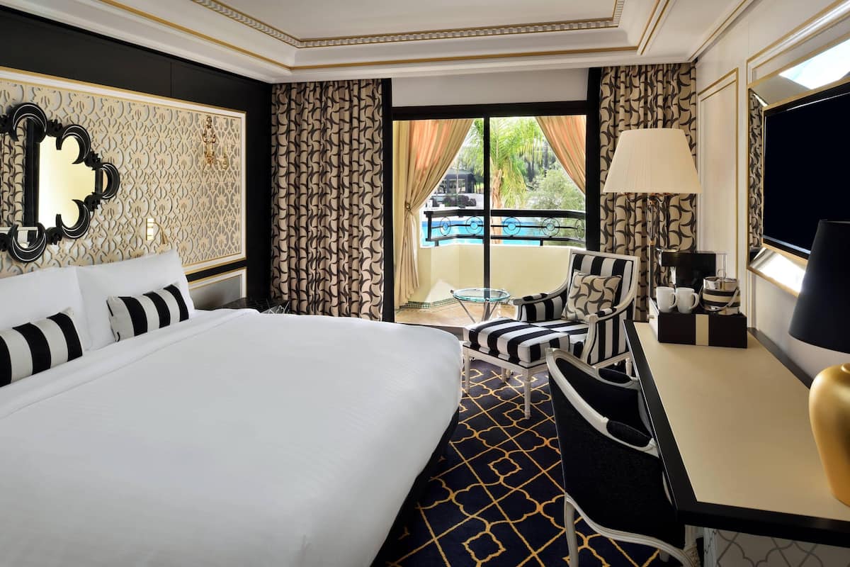 A hotel room with a large bed, a desk with a chair, a TV, and a balcony with a pool view.