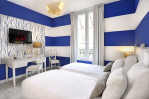 Una habitación de hotel con dos camas, un escritorio, un televisor y una ventana con cortinas.