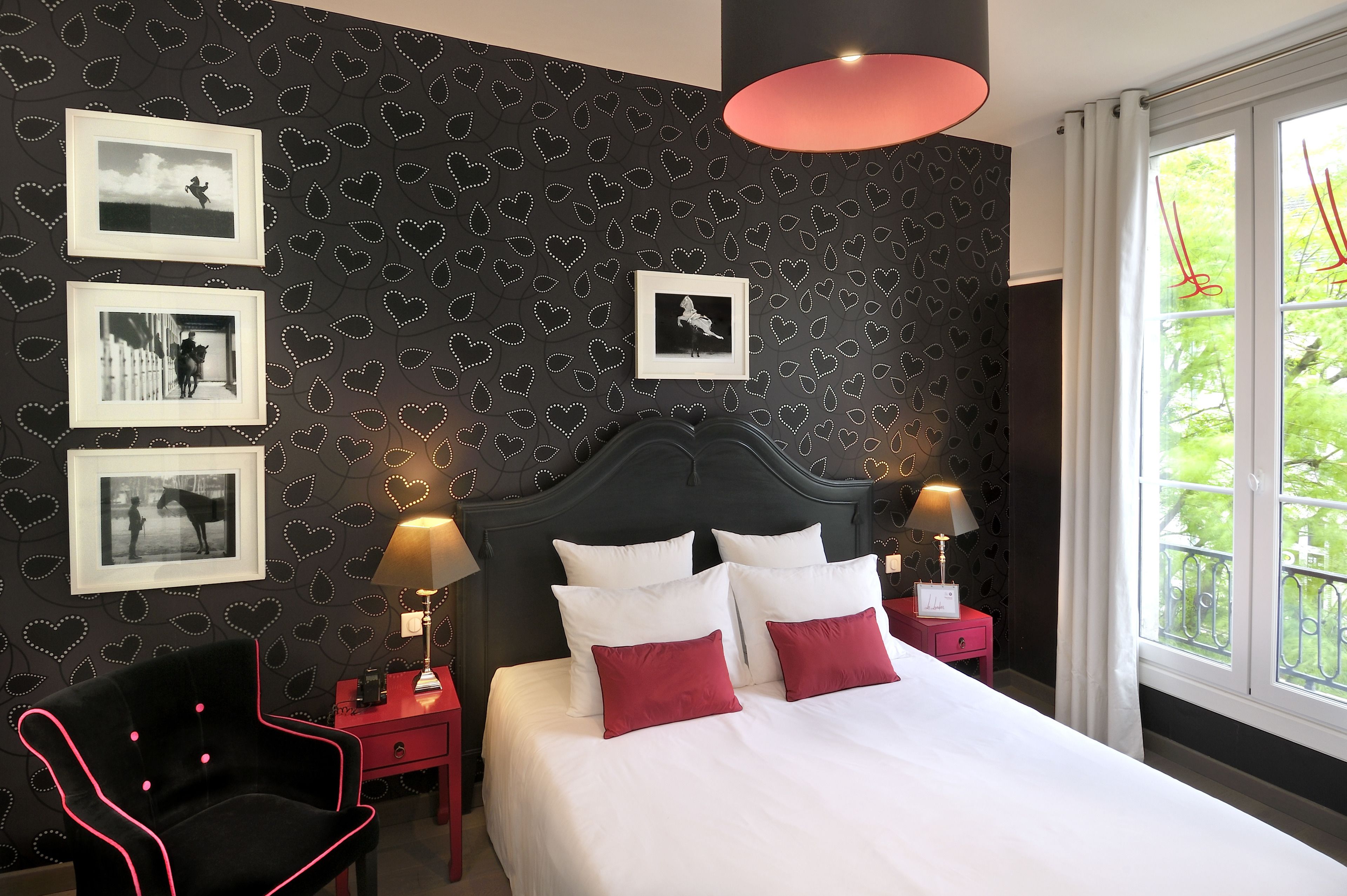 A bedroom with a dark patterned wall, a bed with white and red pillows, and framed pictures on the wall.