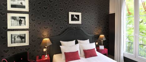 A bedroom with a dark patterned wall, a bed with white and red pillows, and framed pictures on the wall.