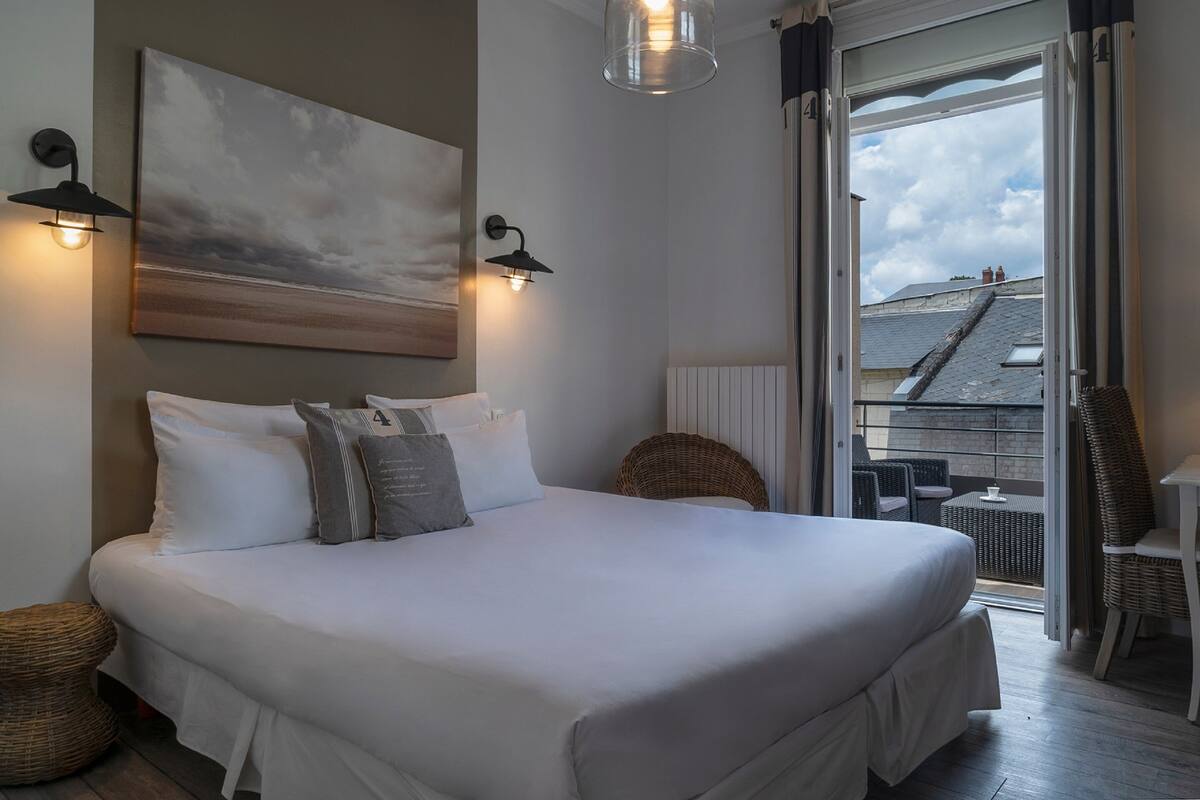 Une chambre avec un grand lit, deux lampes fixées au mur, un tableau et une vue sur le balcon extérieur.