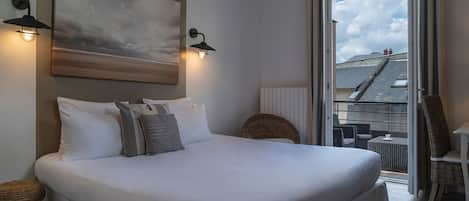 A bedroom with a large bed, two wall-mounted lamps, a painting, and a view of the outside balcony.