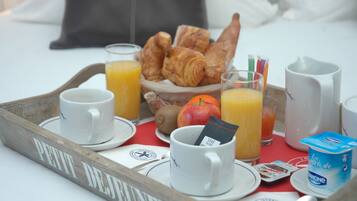 Bandeja de desayuno con croissants, jugo, una taza y un pequeño recipiente de yogur sobre una cama con almohadas.