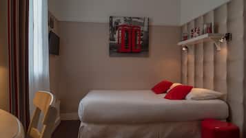 A hotel room with a bed, a red telephone booth artwork, a shelf with books, and a chair.