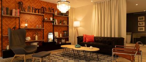 Una sala moderna con una pared de madera, un sofá negro con cojines rojos, una mesa de centro de madera, una silla de metal y una araña.