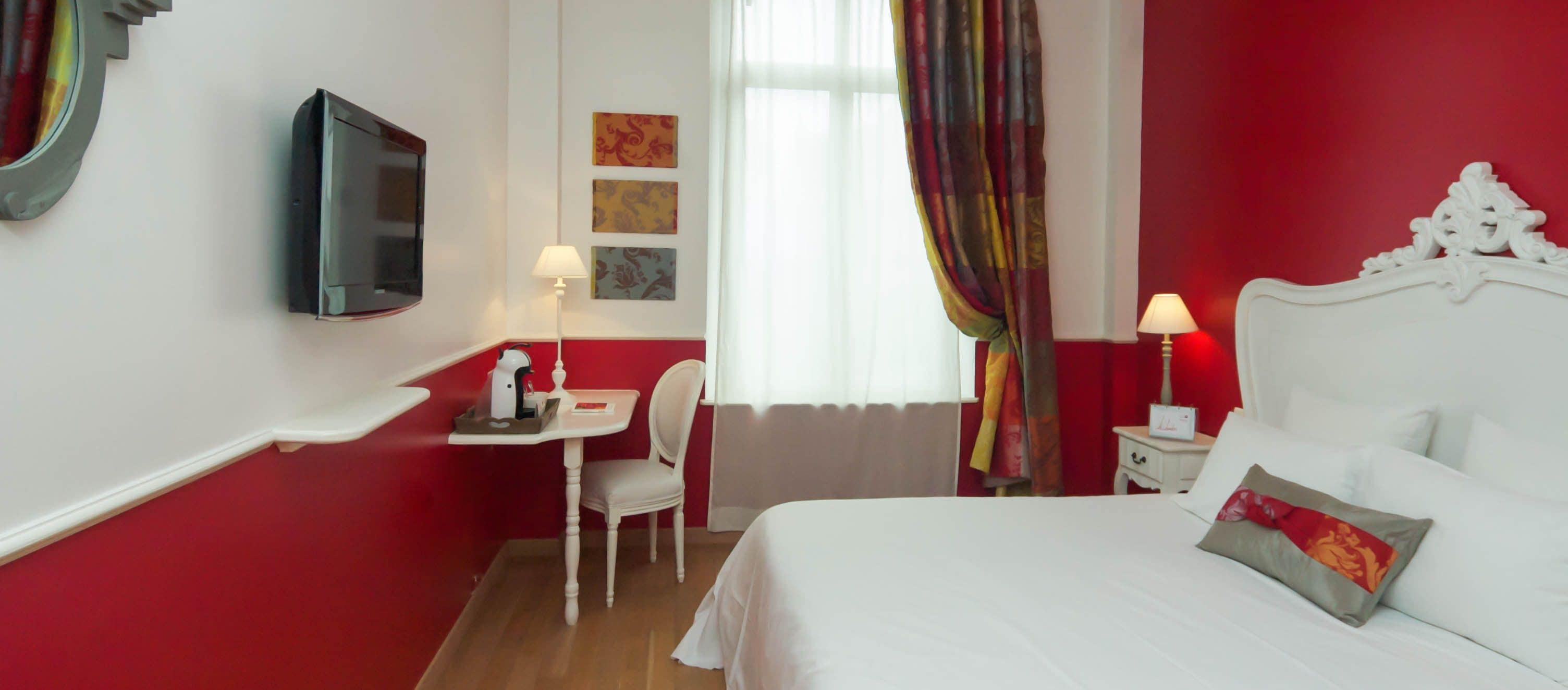A hotel room with a bed, a desk, a chair, a television, and a window with curtains.