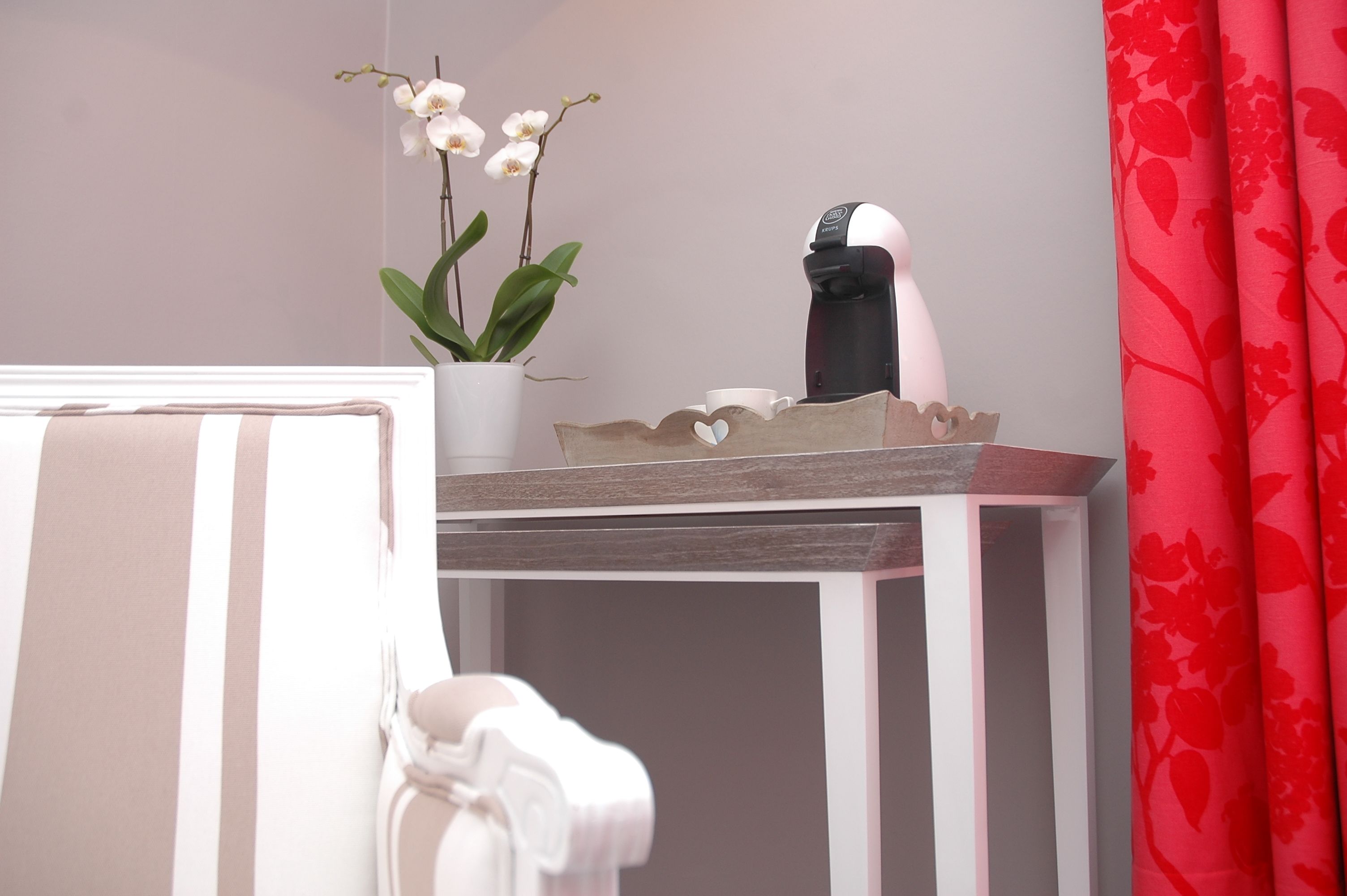 A small table with a coffee maker, a potted orchid, and a cup.