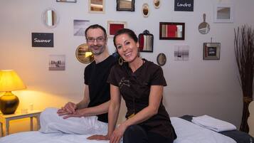 Una pareja sentada en una cama en una habitación con una pared decorada con varios espejos y cuadros.