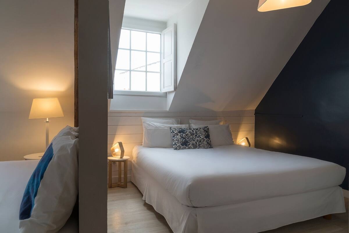 Une chambre à coucher avec un lit, une table de chevet, une lampe et une fenêtre.