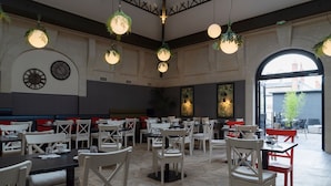 A spacious dining area with multiple tables and chairs, large windows, and hanging spherical light fixtures.
