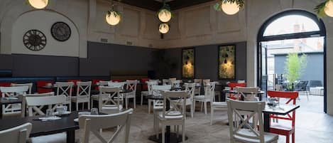 Un amplio comedor con varias mesas y sillas, ventanas grandes y lámparas esféricas colgantes.