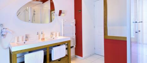 A modern bathroom with a white vanity, a large mirror, a glass shower enclosure, and a red accent wall.