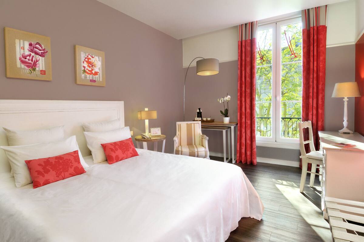 Une chambre d’hôtel avec un grand lit, un bureau avec une chaise, une lampe et deux tableaux accrochés au mur.