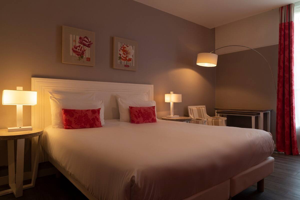 Une chambre d’hôtel avec un grand lit, deux lampes de chevet, un fauteuil et une cheminée.