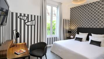 A hotel room with a large bed, a desk with a lamp, a chair, and a window with curtains.