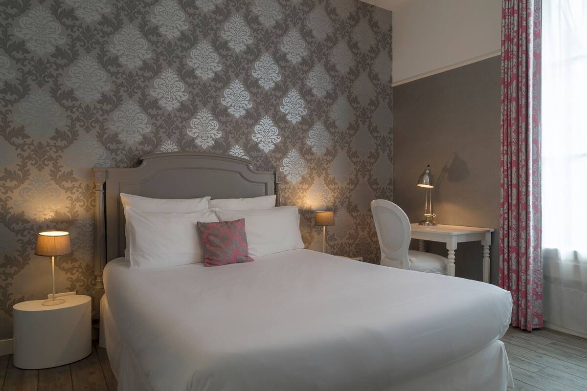 Un lit bien fait, avec du linge de lit blanc et un seul oreiller rose, encadré par deux lampes de chevet.