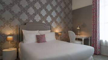 A neatly made bed with white linens and a single pink pillow, flanked by two bedside lamps.