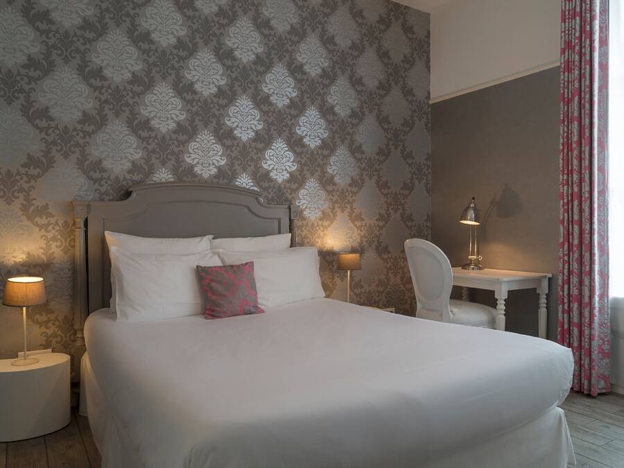 A neatly made bed with white linens and a single pink pillow, flanked by two bedside lamps.