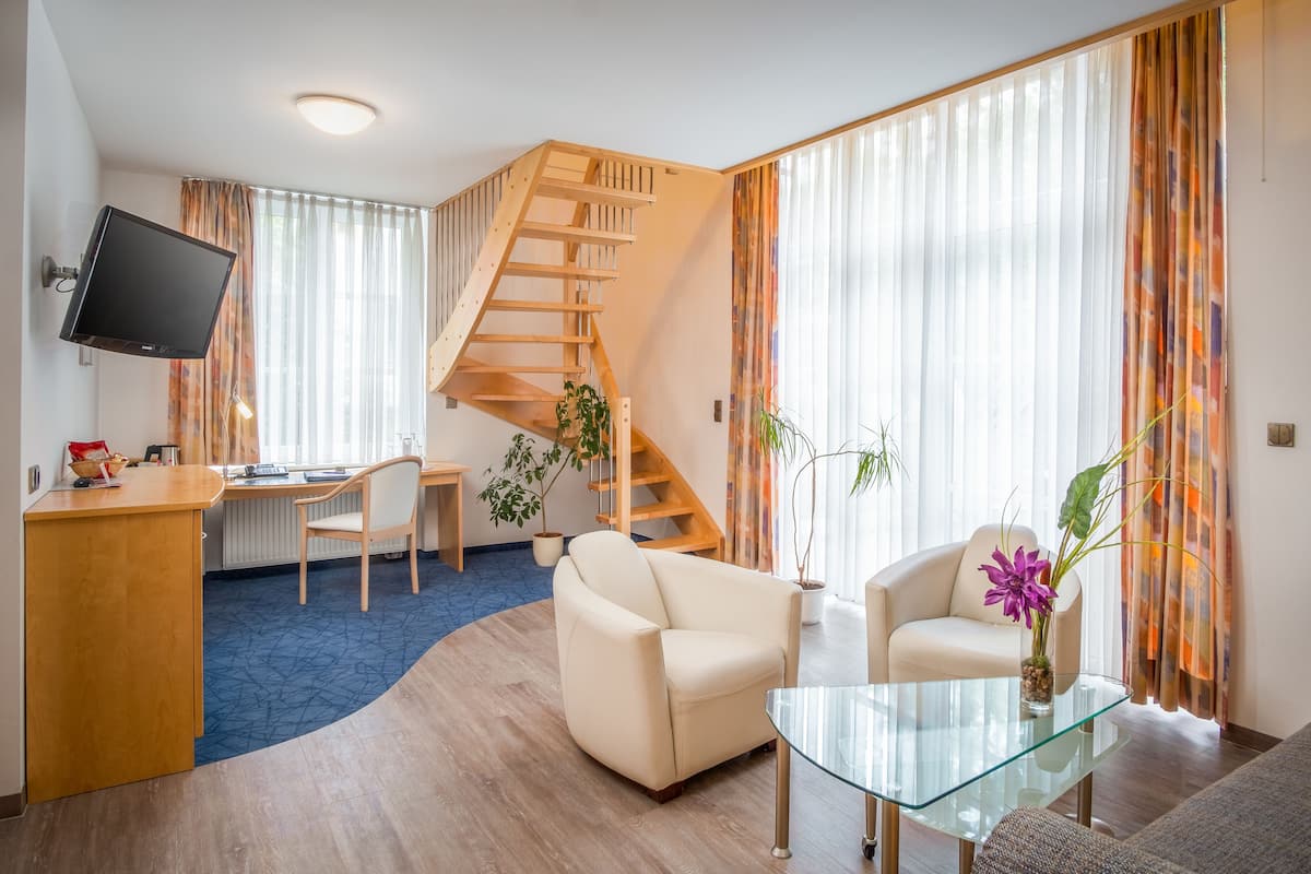 A modern living room with a wooden staircase, a flat-screen TV, a desk, and two sofas.