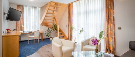 Una sala de estar moderna con una escalera de madera, un televisor de pantalla plana, un escritorio y dos sofás.