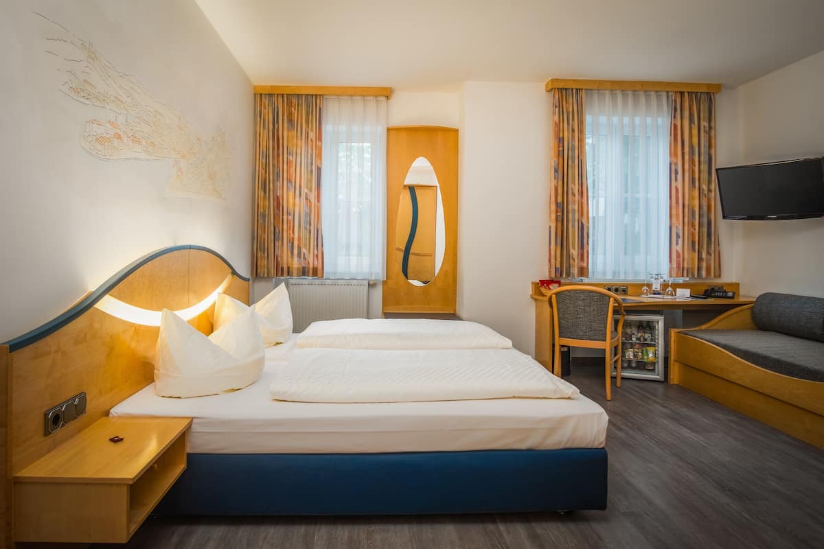 A hotel room with a bed, bedside table, lamp, desk, chair, TV, and a small refrigerator.