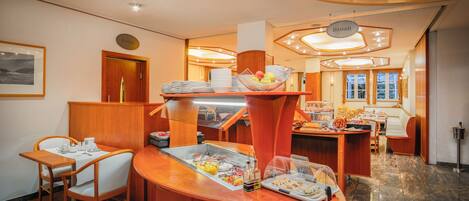 A hotel dining area with a buffet setup, wooden furniture, and a modern interior design.