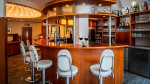 A bar area with a curved wooden counter, bar stools, and shelves stocked with liquor bottles and glasses.