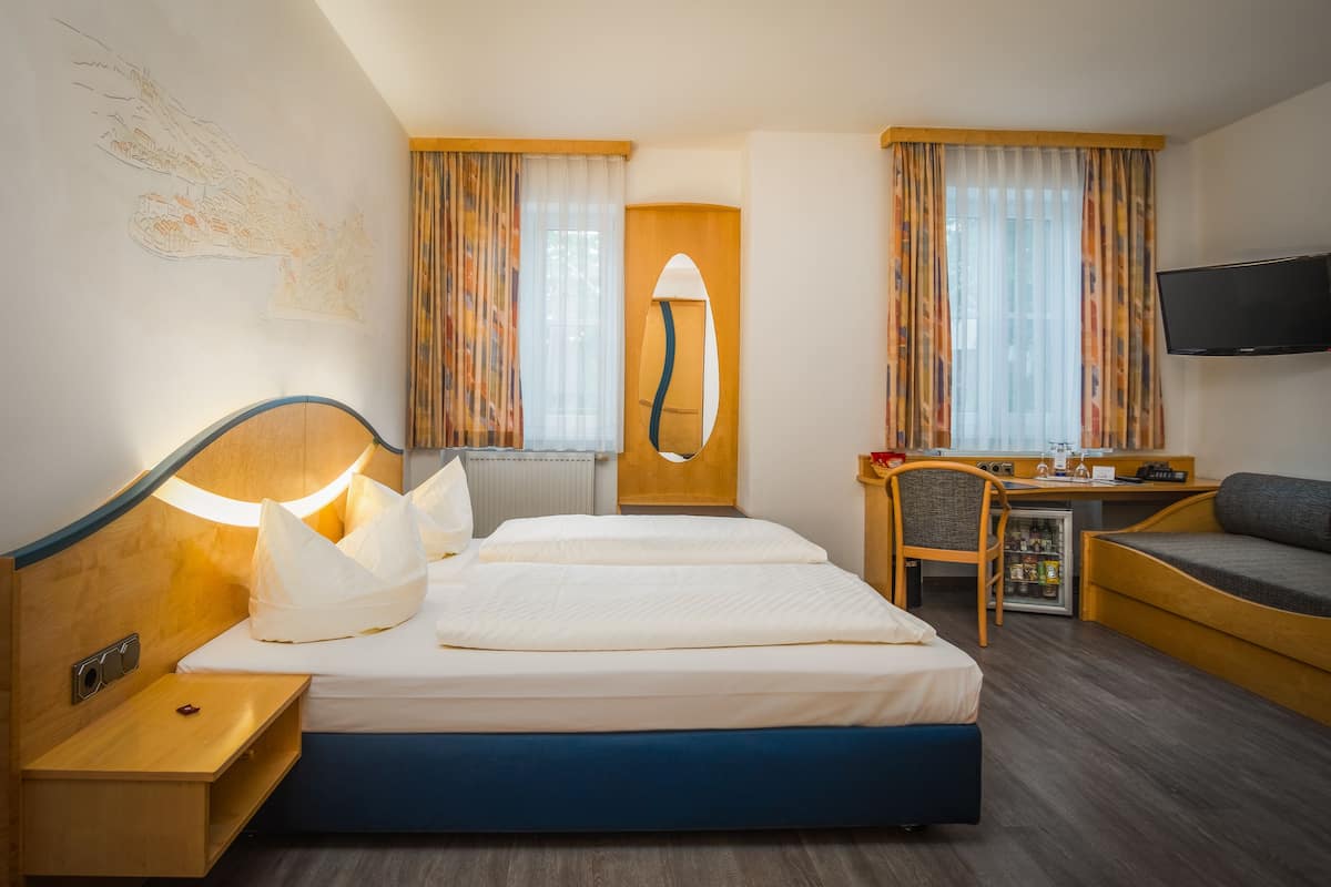 A hotel room with a bed, a desk with a chair, a TV, and a small refrigerator.