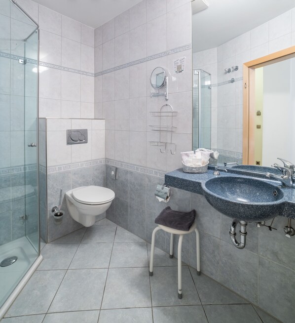 Une salle de bain moderne avec une douche à parois de verre, des toilettes, un lavabo avec un miroir et un petit tabouret.