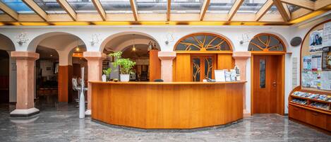 A reception area with a wooden reception desk, arched columns, and a glass ceiling.