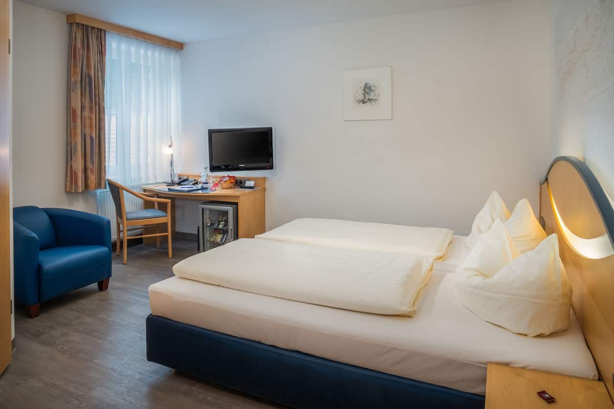 A hotel room with a bed, a desk with a computer, a chair, and a television.