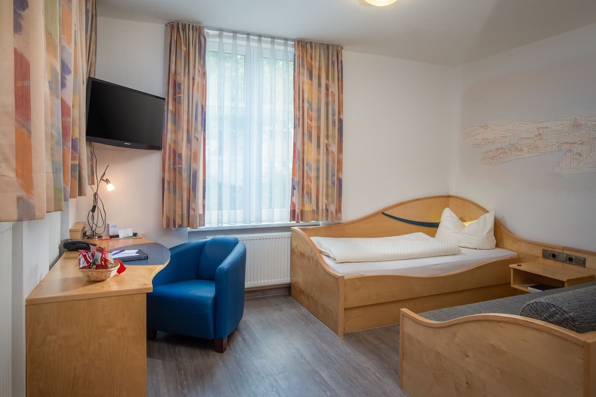 A hotel room with a wooden bed, a desk with a chair, a television, and a window with curtains.