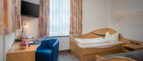 Una habitación de hotel con una cama de madera, un escritorio con una silla, un televisor y una ventana con cortinas.