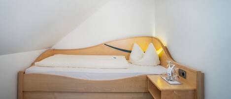 Un lit en bois avec une tête de lit, une table de chevet avec une lampe et une petite étagère avec des lunettes et un livre.